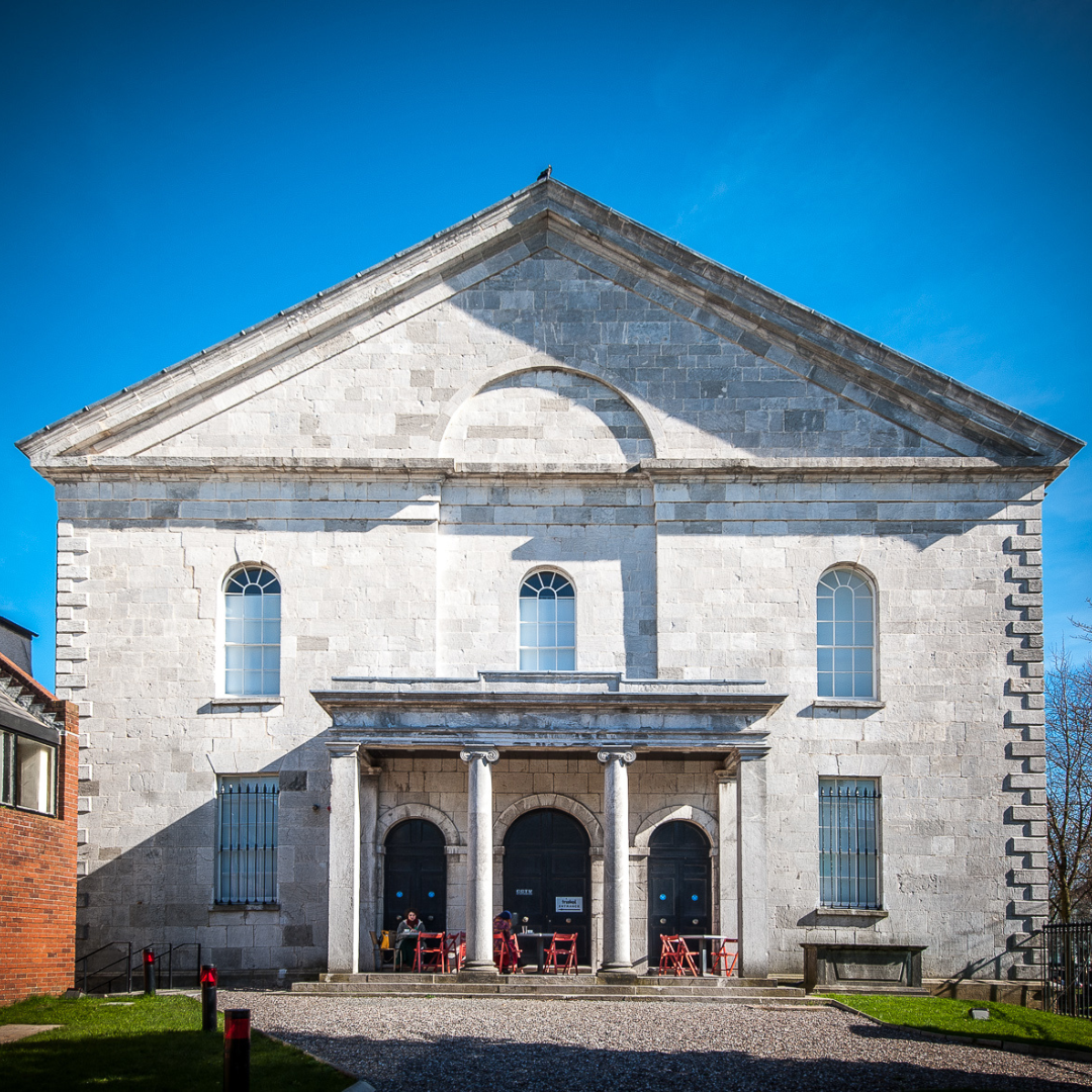 The exterior of Triskel Christchurch in Cork, with pale stone fa&ccedil;ade, columns and courtyard seating in front.